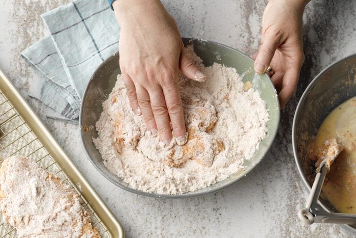 Chicken being dredged in a mixture of flour, garlic powder, onion powder, paprika, pepper and salt. A hand can be seen patting the chicken.